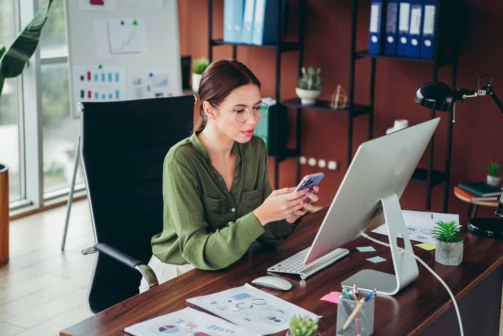 A,Focused,Young,Professional,Woman,Uses,Her,Smartphone,And,Desktop